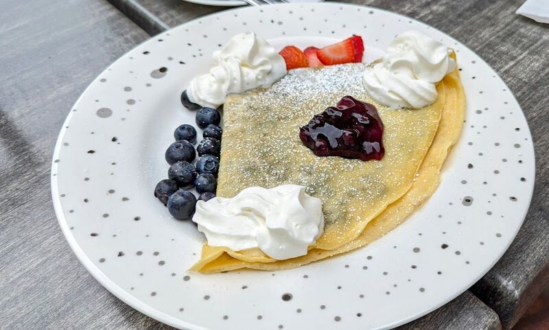 Sweet crêpe with blueberries, strawberries, berry compote and whipped cream on a speckled plate