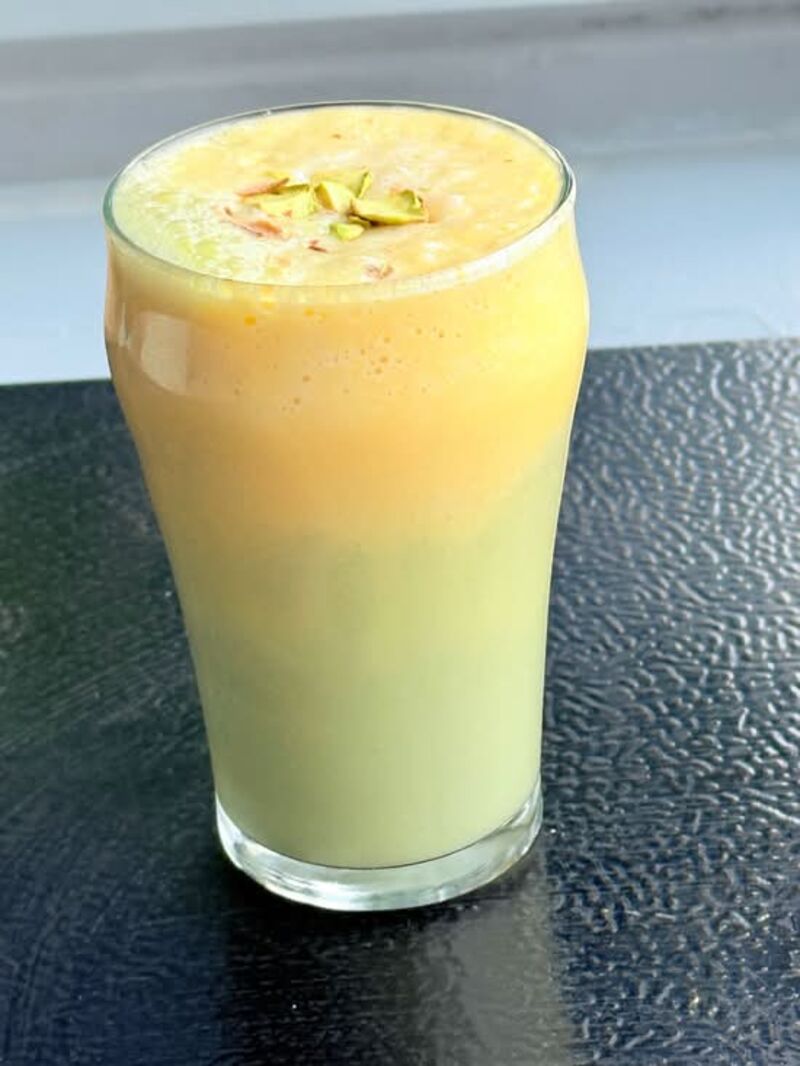 Mango pistachio smoothie in a tall glass topped with chopped pistachios