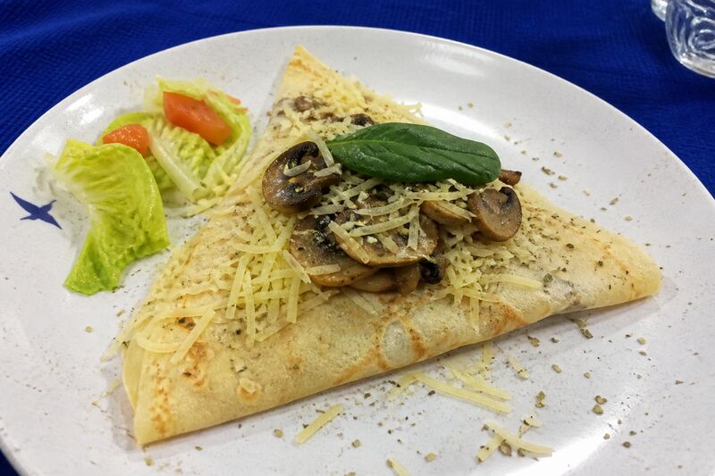 Savoury crêpe folded with mushrooms, cheese and spinach on a white plate